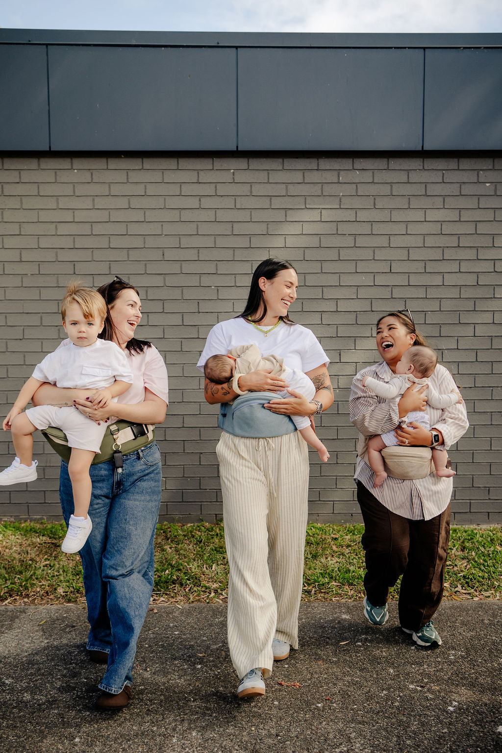 Three mums laughing while carrying a toddler and babies on HipSurfer hip seat carriers